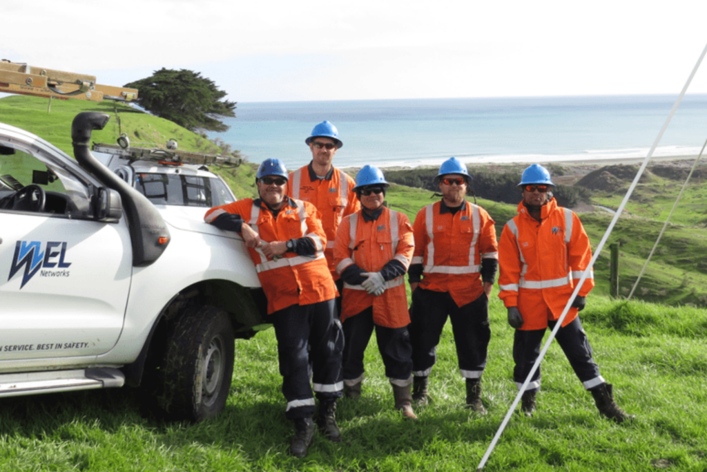 photo of employees working at wel networks in high vis vests standing next to a car and grass